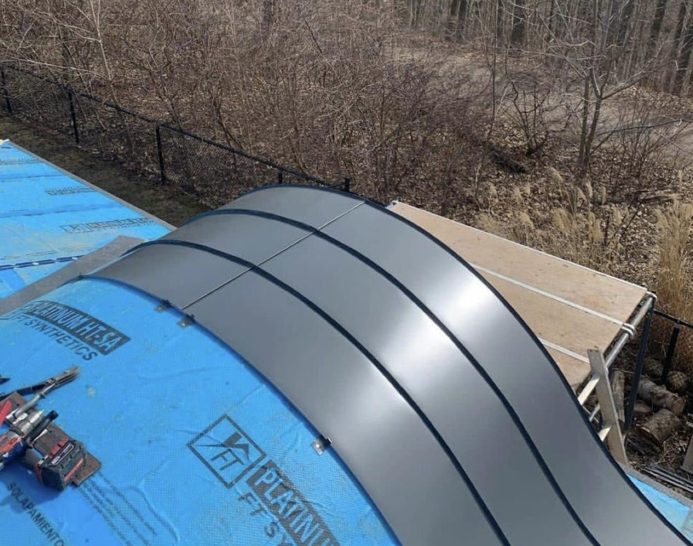 Standing seam metal panels being installed on a curved roof section — Shelby Roofing Services