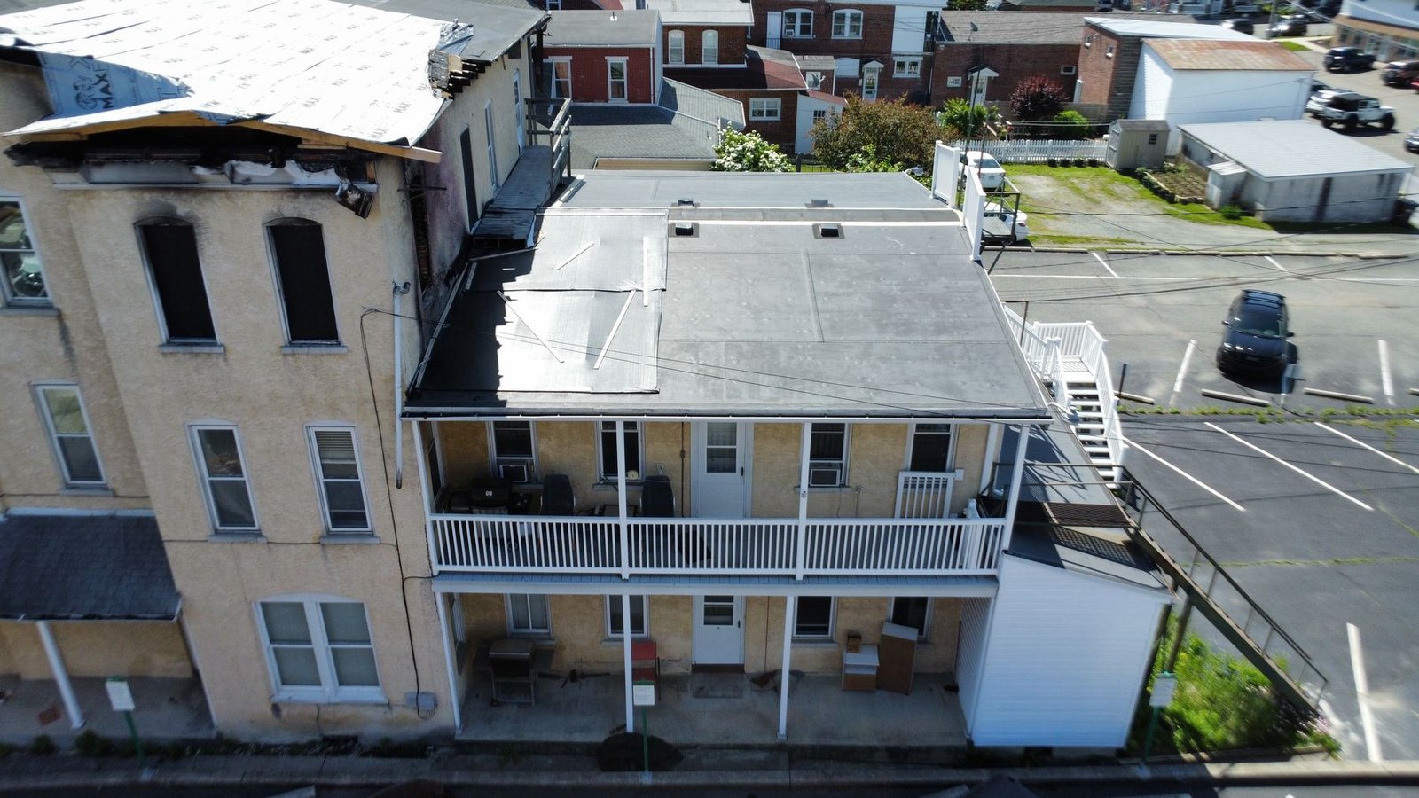 Before — rear aerial showing full extent of flat roof failure and fire-damaged neighboring structure, PA