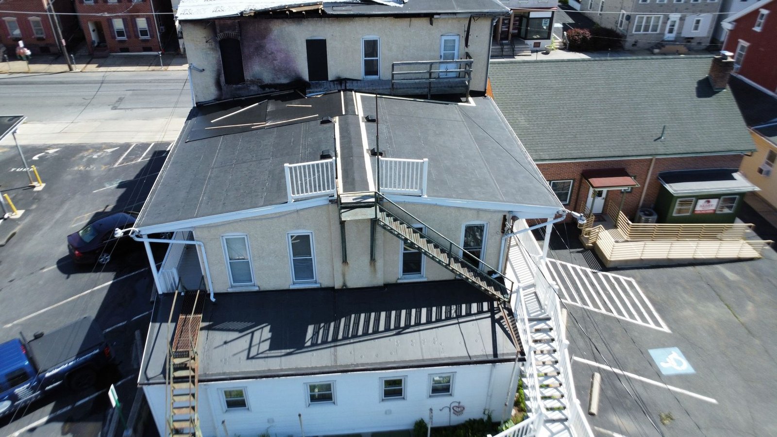 Before — side aerial showing main building with deteriorated flat roof and fire-damaged neighbor, PA