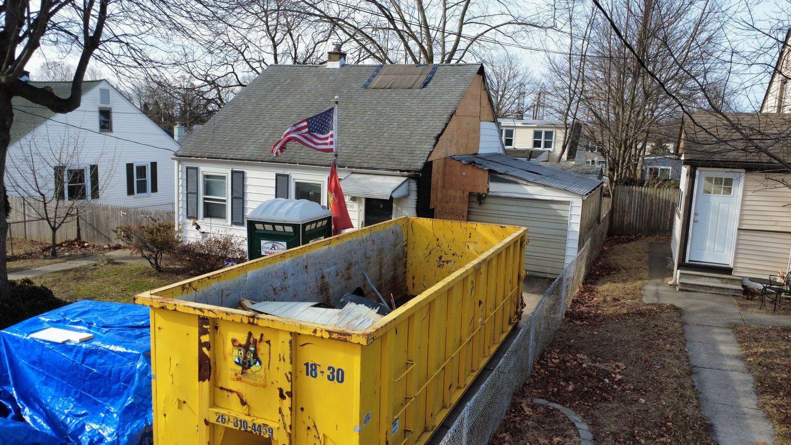 Before — front of Cape Cod bungalow with old gray shingles and Shelby dumpster, NJ