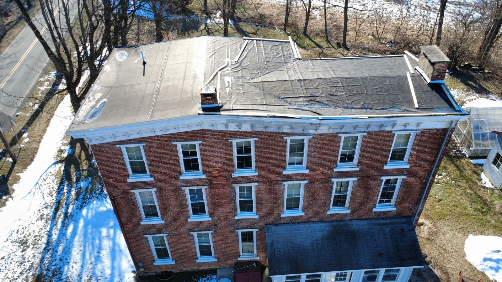 Before — top-down aerial of 3-story brick building with deteriorated flat rubber roof and snow, PA
