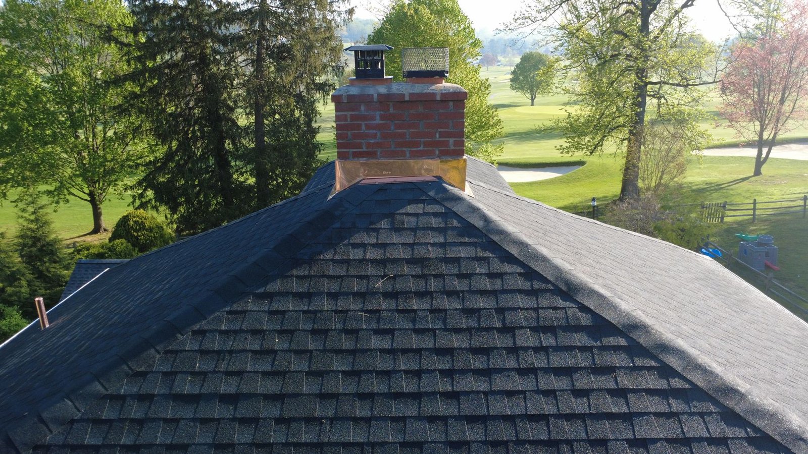After — aerial of completed blue colonial showing new dark shingles and copper chimney with golf course setting — Shelby Roofing Services PA