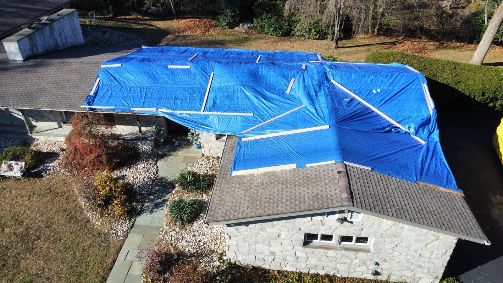 Emergency blue tarp covering storm-damaged roof — aerial drone view